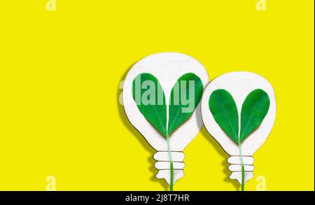 Flat wooden lightbulb shapes with fresh green leaves isolated on a yellow background. Sustainable green power technologies. Stock Photo