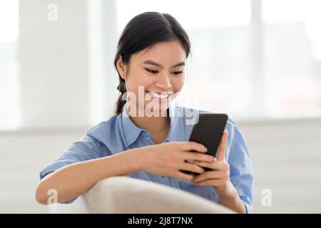 Smiling lady sitting on sofa, using cell phone, closeup Stock Photo