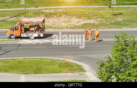 drawing road markings on the road on a sunny summer day. Workers in orange suits on the road. Road safety Stock Photo