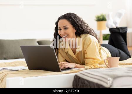 Smiling woman using laptop lying on bed at home Stock Photo
