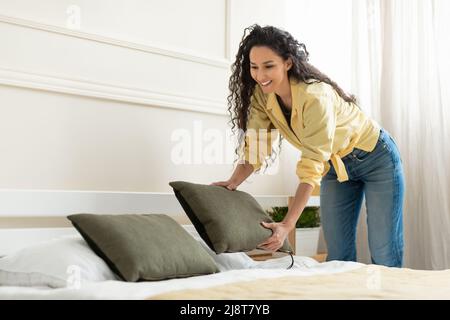 Happy millennial young woman making bed after wake up Stock Photo