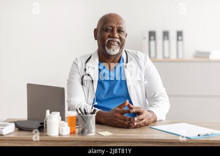 Portrait of smiling doctor looking at camera sitting at desk Stock Photo