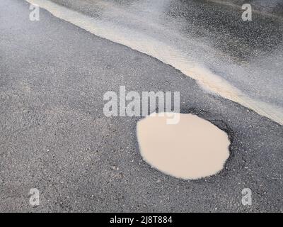 Hole and puddle on bad broken road. destroyed Road with Puddle. Bad road. Puddles and dirt on dirt road. Stock Photo