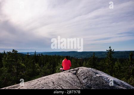 Woman sitting on a rock with beautiful summer landscape from Ukko-Koli, Koli National Park in Finland Stock Photo