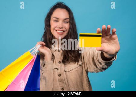 Glad young european brunette female with purchases bags showing credit card isolated on blue background Stock Photo