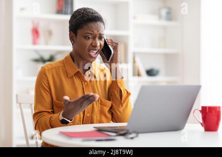 Furious black businesswoman fighting on phone, office interior Stock Photo