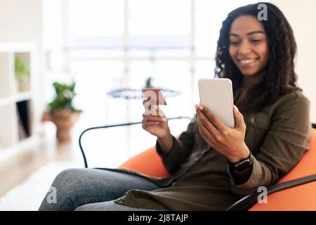 Smiling black lady using cellphone and credit card at home Stock Photo