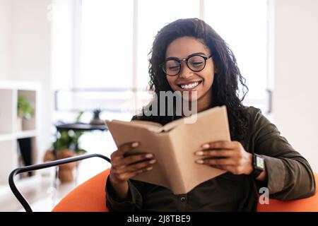Smiling black woman in glasses reading book Stock Photo