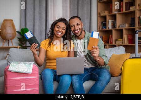 Loving black spouses planning trip, using laptop and booking hotel, having tickets, sitting with packed clothes Stock Photo