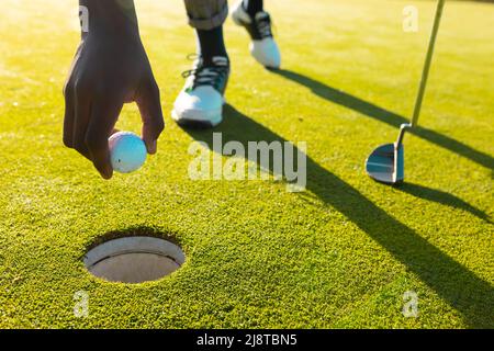 Cropped image of african american young man putting golf ball in hole at golf course in summer Stock Photo
