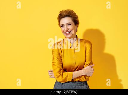 Positive happy woman. Photo of kind elderly woman in yellow shirt on yellow background Stock Photo