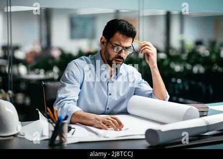 Concentrated busy smart attractive young arab man engineer with beard in shirt, glasses thinking about project Stock Photo