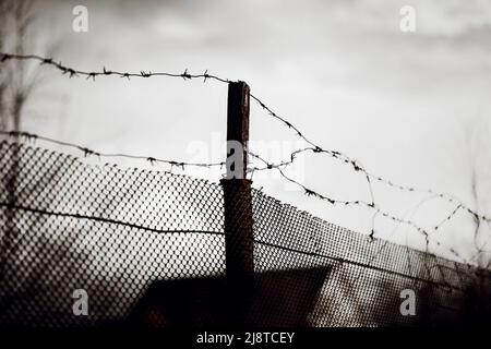 An old mesh fence with barbed wire wound on top in cloudy sad weather. Prison and war. Stock Photo