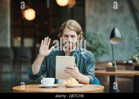 Portrait of serious modern guy with beard sitting at round table in loft cafe and calling by mobile phone Stock Photo