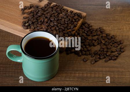 Green cup of coffee with coffee beans on wooden background Stock Photo