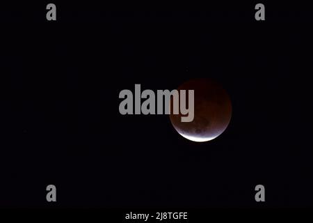 The end of the Flower Blood Moon lunar eclipse of May 15th and 16th 2022, as the moon starts to receive sunlight again. Stock Photo