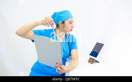 beautiful woman doctor, wearing blue uniform and blue surgical cap, stethoscope on her neck, using the tablet to show results, on white background Stock Photo