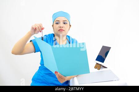 beautiful woman doctor, wearing blue uniform and blue surgical cap, stethoscope on her neck, using the tablet to show results, on white background Stock Photo