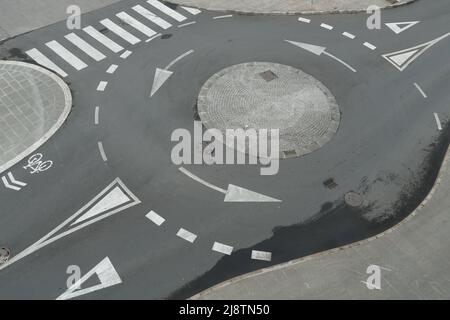Aerial view from top on empty traffic circle or roundabout road with white arrows, crosswalk and other road signaling or marking in European town. Stock Photo