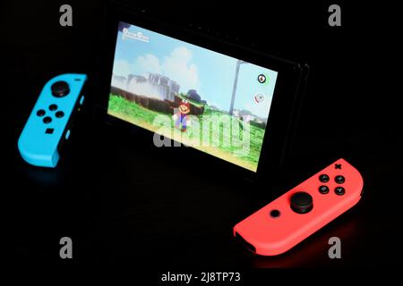 Nintendo Switch with Super Mario Odyssey on a screen, selective focus. Video game console in handheld mode with the Joy-Con on black background Stock Photo