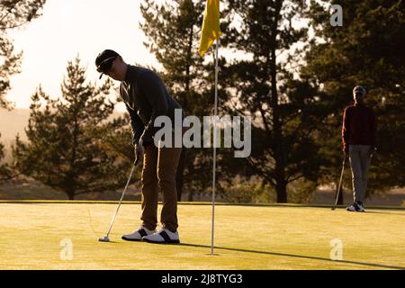 Caucasian young man playing golf with african american young male friend at golf course at sunset Stock Photo