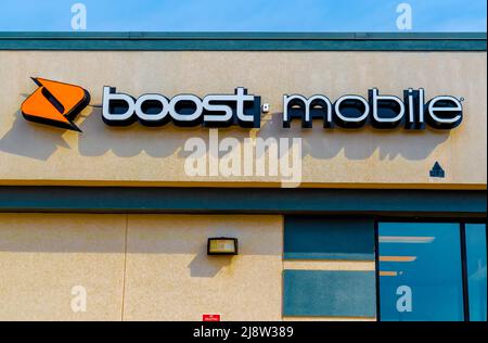 Outside, 'Boost Mobile' facade brand and logo signage above glass windows in soft early morning light on a sunny day with orange logo in Charlotte, NC. Stock Photo