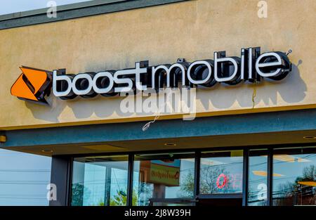 Outside, 'Boost Mobile' facade brand and logo signage above glass windows in soft early morning light on a sunny day with orange logo in Charlotte, NC. Stock Photo