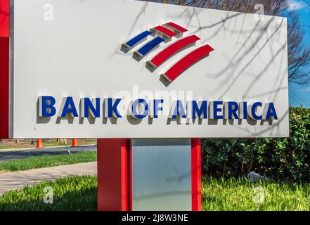 Outdoor, free standing 'Bank of America' brand and logo sign in red, white and blue with greenery and reflections on a sunny day. Stock Photo