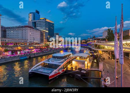 Wien, Vienna: river Donaukanal (Danube Canal), people sit on bank reinforcement, outdoor restaurants and bars, Schwedenplatz boat terminal, Sofitel ho