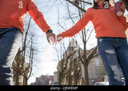 Love and date concept. Close up of young lover man and woman in jeans overalls holding hands while walking on street Stock Photo