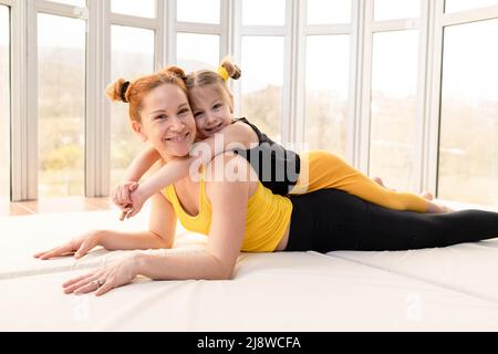 Little girl lying on top of her fit mother in the gym Stock Photo