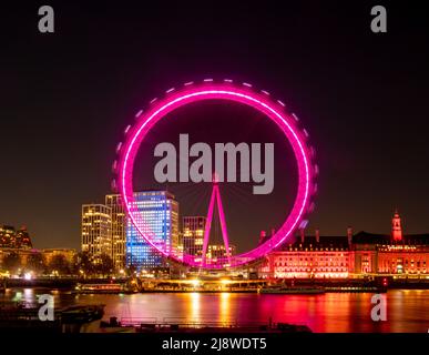 The London Eye at night, illuminated with pink light, situated along The Queen's Walk. London. Stock Photo