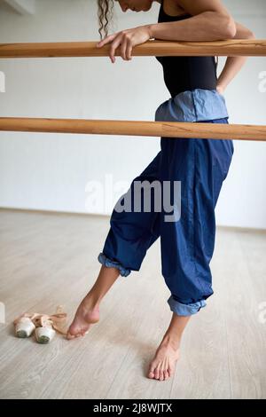 Young female ballet dancer in rolled baggy pants rehearsing dance in studio Stock Photo