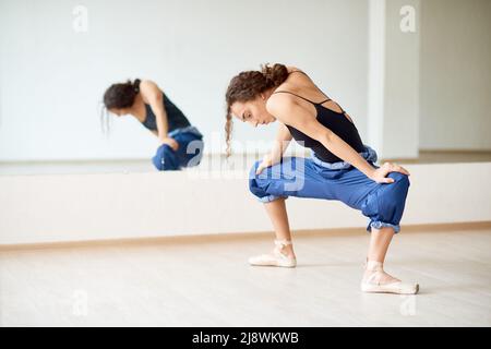 Young female ballet dancer stretching her body before rehearsal in dancing hall Stock Photo