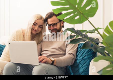 Mid aged european joyful couple sitting on a couch holding a laptop doing online shopping. High quality photo Stock Photo