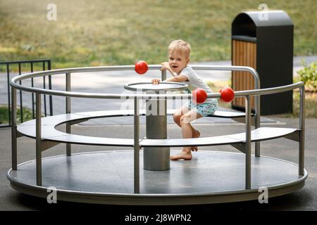 The boy is spinning on the carousel at the playground. Circular metal rotational swing. Stock Photo