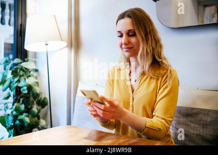young attractive blonde woman with yellow shirt using her smart phone in a cafe Stock Photo