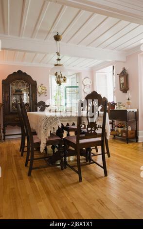 Antique table, high back chairs and furnishings in dining room inside old 1831 Canadiana cottage style quarry stone home. Stock Photo