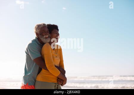 Cheerful african american bearded senior man embracing mature woman against sea and blue sky Stock Photo