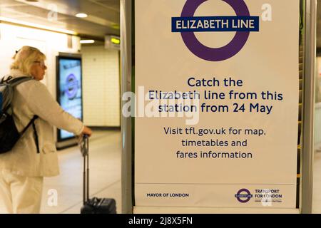 Woman looks at a poster informing passengers that 'catch the Elizabeth line from this station from 24 May' at London underground station England UK Stock Photo
