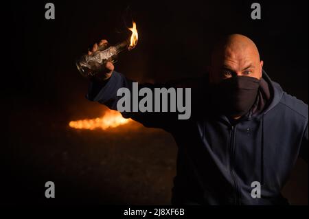 A masked man is holding a burning bottle. Molotov cocktail. Stock Photo