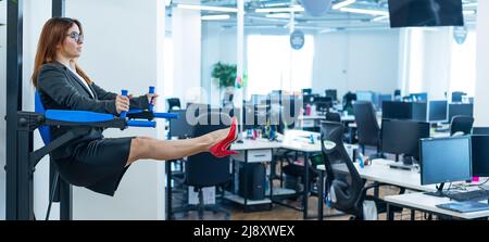 Business woman doing exercises on the mounted horizontal bar in the office. Sports during a break at work. Stock Photo