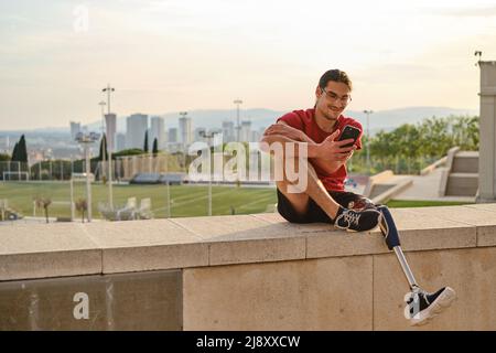 Young man with a disability using a mobile phone while relaxing sitting outdoors. Stock Photo