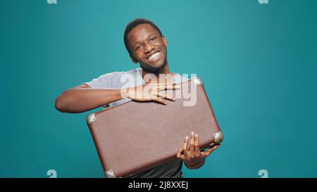 Happy man holding suitcase feeling excited about vacation voyage, leaving to go abroad on travel adventure. Cheerful model with briefcase luggage preparing for tourist holiday trip. Stock Photo
