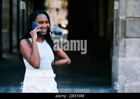 Smiling African American woman talking on the phone while standing outdoors. Stock Photo