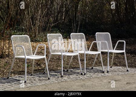 empty white metal grid chairs in line in the garden area in the springtime Stock Photo