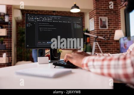 Closeup of system developer writing code on personal computer typing algorithm on keyboard working remote. African american programmer coding from home developing software on pc. Stock Photo