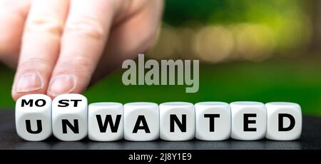 Hand turns dice and changes the expression "unwanted" to "most wanted". Stock Photo