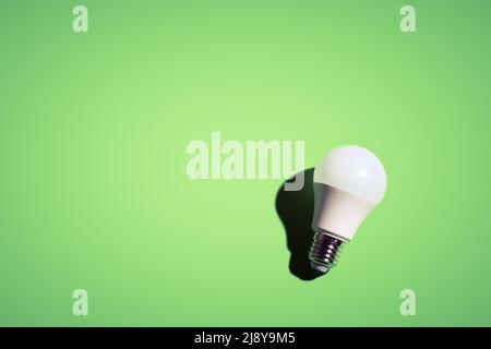 White lightbulb on green background under the bright light with black shadow. Stock Photo