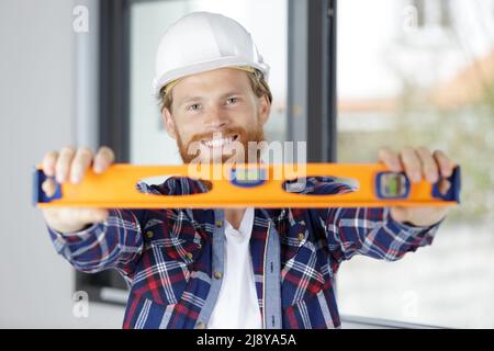 smiling builder in a hardhat using a spirit level Stock Photo